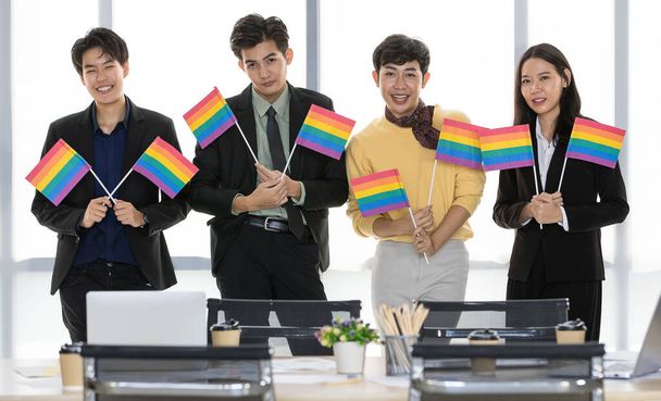 ΛΟΑΤ ασιατική εκτελεστική επιχειρηματική ομάδα χαμόγελο, χαρούμενος, και να απολαύσετε τη συνεργασία με την ανύψωση συμβολική σημαία ουράνιο τόξο ως σύμμαχος ομάδα για την υποστήριξη των διεμφυλικών δικαιωμάτων κίνημα και την κοινότητα κατά τη συνάντηση στο γραφείο - Φωτογραφία, εικόνα