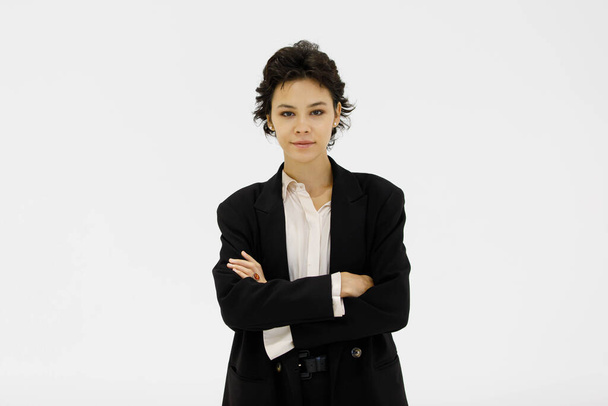 Pewna siebie kobieta przedsiębiorca w czarnym garniturze formalnym stojąca z skrzyżowanymi ramionami na białym tle w studio i patrząca w kamerę - Zdjęcie, obraz