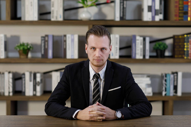 Serious frowning male entrepreneur in classy suit  making decision while looking at camera and sitting at table in office - Foto, Bild