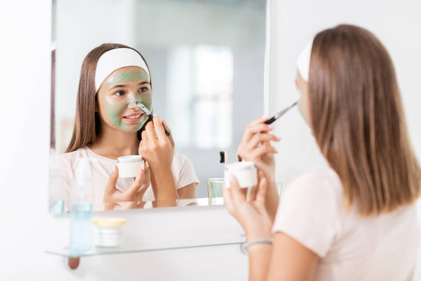 teenage girl applying mask to face at bathroom - Foto, Imagem