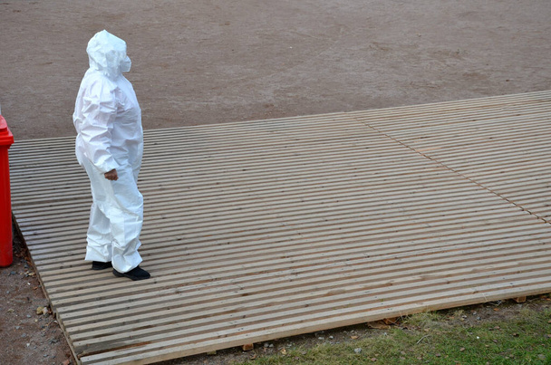 Arbeiter in weißem Schutzanzug gegen Infektionskrankheiten stehen auf einem hygienischen Holzgitter. Untersuchung der Patienten draußen auf der Straße und im Park. führt Impfungen und Tests durch - Foto, Bild