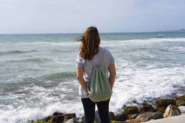 Malownicze ujęcie kobiety stojącej z tyłu na brzegu i patrzącej na fale oceanu. - Zdjęcie, obraz