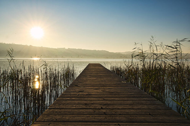 A wooden deck at the shore of a lake in Sempach, Switzerland, surrounded by mountains - Foto, Bild