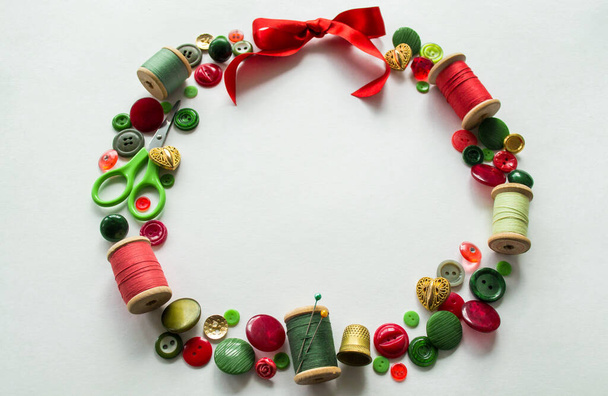 Weihnachtskranz aus Knöpfen, Fäden, Nadeln, Scheren, Fingerhut rot, grün und gold. Weißer Hintergrund. Kopierraum. - Foto, Bild