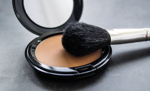 Detailní záběr na černý make-up štětec vedle otevřené krabice se zrcadlem a pudrem a růžovým práškem. Černé pozadí. - Fotografie, Obrázek