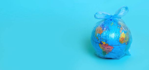 Koncepcja ekologii i problem zanieczyszczenia środowiska. Baner Earth globus w plastikowej torbie na niebieskim tle.  - Zdjęcie, obraz