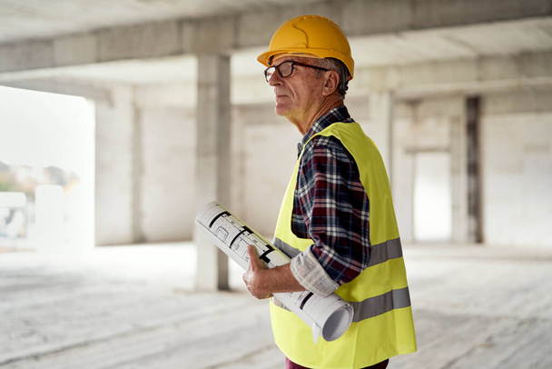 Caucasian senior engineer walking and holding plans on construction site - Foto, Bild