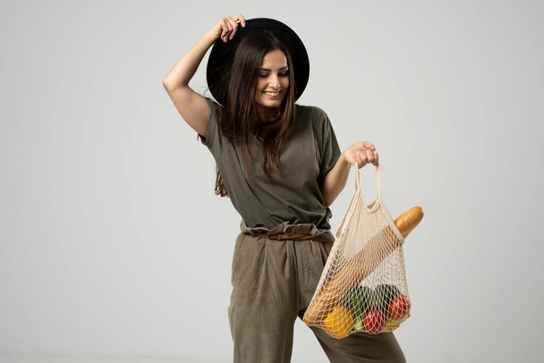 A modern stylish woman with a mesh shopping bag with vegetables against the background of the studio. The concept of healthy nutrition, vegetarianism and ecology. Refusal of plastic bags. - Foto, Imagem
