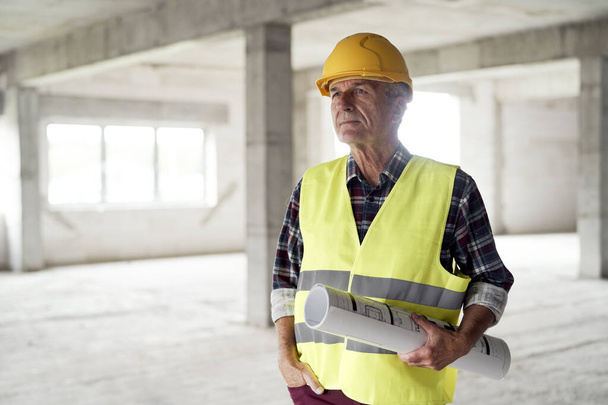 Caucasian senior engineer holding plans and standing on construction site - Photo, Image