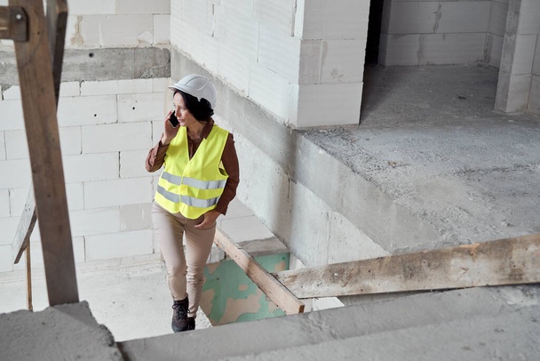 Cintura video di ingegnere caucasico donna sul cantiere a parlare al telefono e controllare alcuni documenti - Foto, immagini
