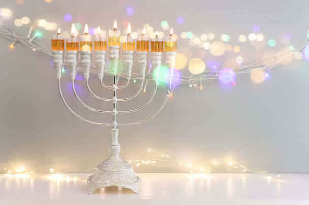 Image of jewish holiday Hanukkah with menorah (traditional candelabra) and oil candles over garland glitter lights background - Fotó, kép