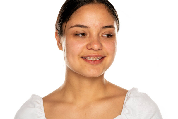 una joven sonriente sin maquillaje mira hacia otro lado sobre un fondo blanco - Foto, imagen