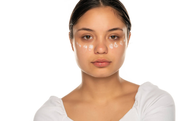 een jonge serieuze vrouw poseren met gezichtscrème op een witte achtergrond - Foto, afbeelding