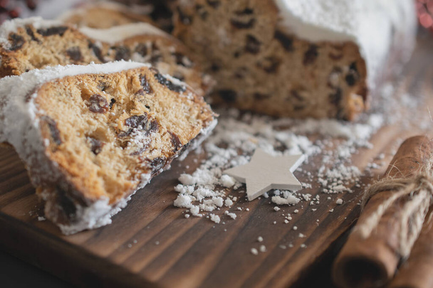 Traditional Christmas stollen made of dried fruits and nuts sprinkled with powdered sugar on the background of a Christmas decor with candles. Traditional Christmas cupcake. - Foto, immagini