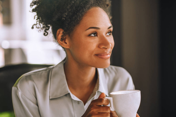 Mooie glimlachende mulatta met koffie en een positief gevoel - Foto, afbeelding