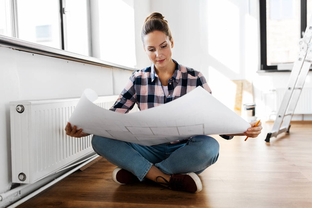 woman with blueprint sitting on floor at home - Photo, Image