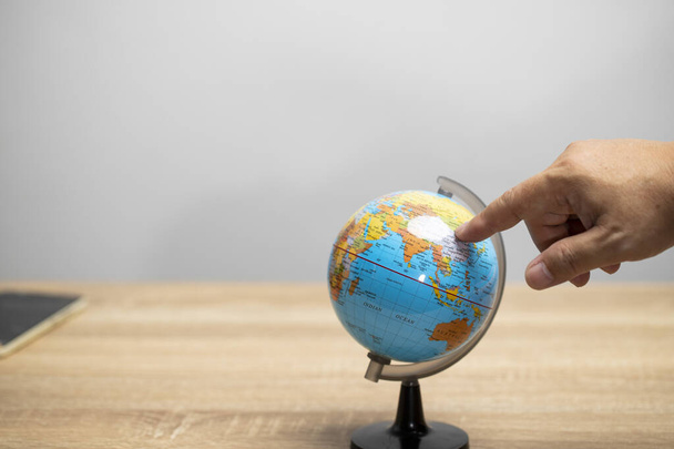 Hand point on the world model stand on brown table with white background copy space to search the world map. - Foto, afbeelding