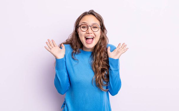 hispanic pretty woman looking happy and excited, shocked with an unexpected surprise with both hands open next to face - 写真・画像