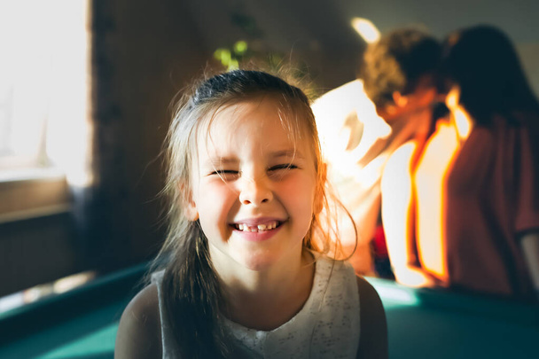 A portrait of a smiling little girl in front of her kissing parents. - Fotó, kép