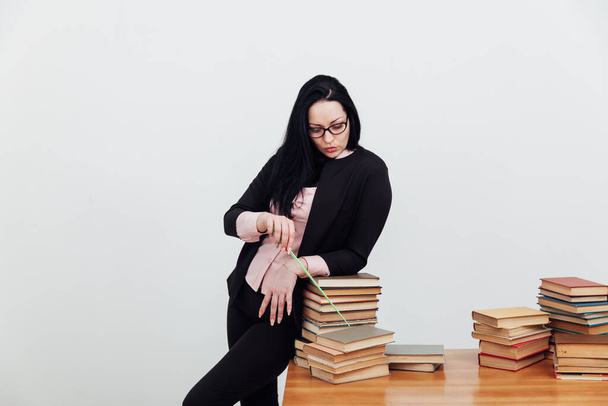 красивая брюнетка в деловом костюме учительница с книгами за столом - Фото, изображение