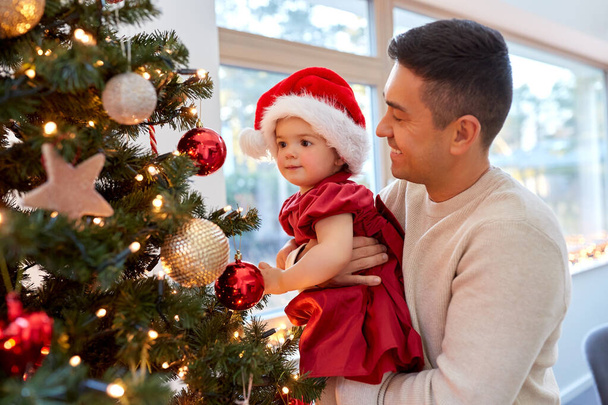 幸せな父親と赤ちゃんの女の子はクリスマスツリーを飾る - 写真・画像