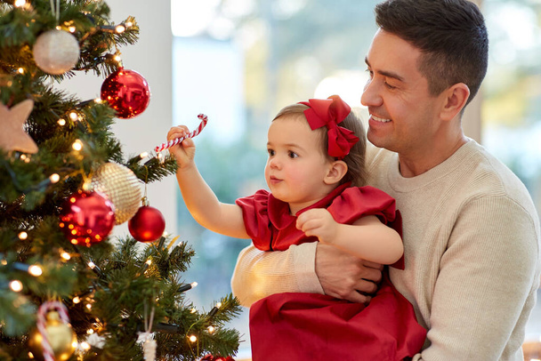 幸せな父親と赤ちゃんの女の子はクリスマスツリーを飾る - 写真・画像