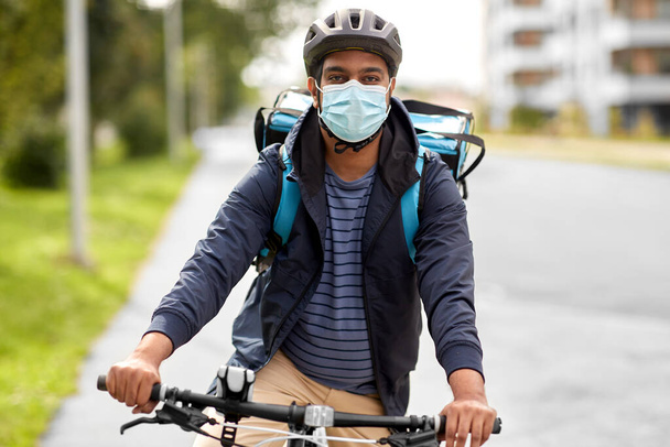 delivery man in mask with smatphone riding bicycle - Photo, image
