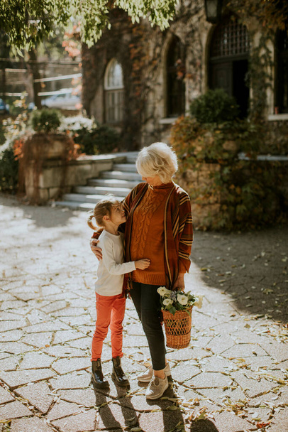 Avó se divertindo com sua pequena neta bonito e segurando cesta cheia de flores - Foto, Imagem