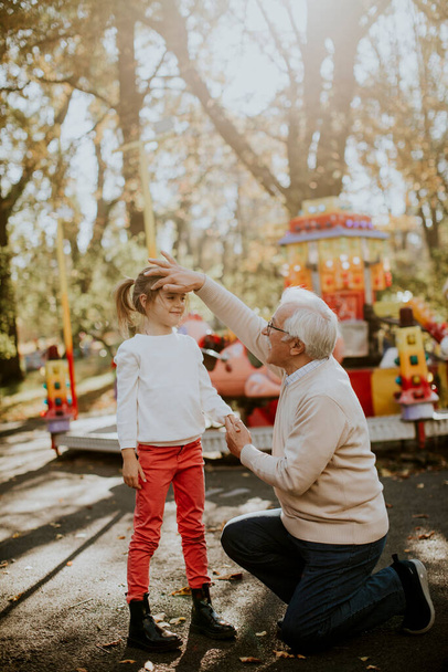 Grandfather having fun with his cute little granddaughter in the amusement park - Photo, Image
