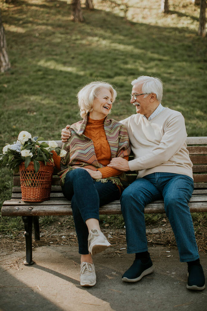 Hermosa pareja de ancianos sentados en el banco con la cesta llena de flores y abrazos - Foto, imagen