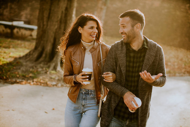 Przystojna młoda para spaceruje w jesiennym parku z kawą na filiżankę w dłoniach - Zdjęcie, obraz