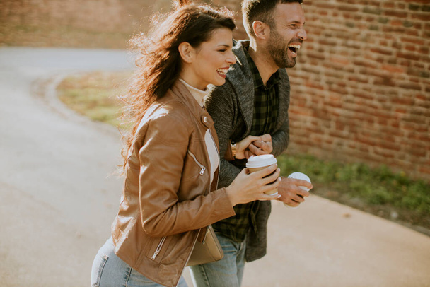 Handsome young couple walking in autumn park with coffee to go cups in hands - Photo, Image