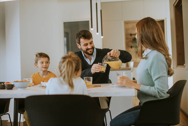 Jong gelukkig gezin praten tijdens het ontbijt aan tafel in appartement - Foto, afbeelding