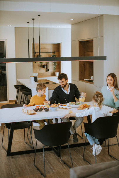 Jeune famille heureuse parlant tout en déjeunant à table à l'appartement - Photo, image
