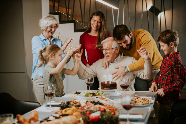 Gelukkige familie viert grootvader verjaardag met taart en kaarsen thuis - Foto, afbeelding