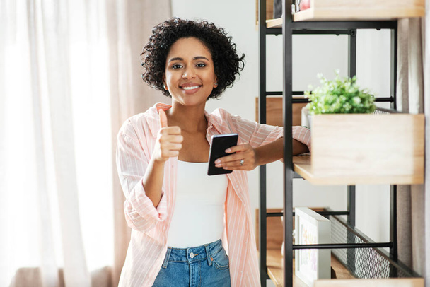 woman with smartphone showing thumbs up at home - Foto, Imagem