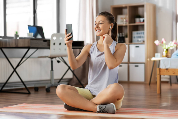 girl with phone and earphones exercising at home - Фото, изображение