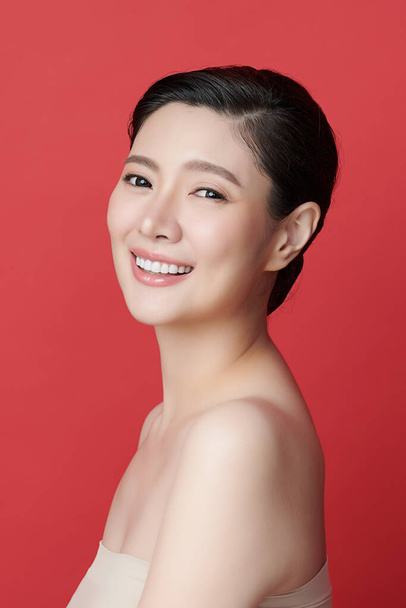 Schöne junge asiatische Frau mit sauberer, frischer Haut auf rotem Hintergrund, Gesichtspflege, Gesichtsbehandlung, Kosmetologie, Schönheit und Wellness, asiatische Frauenporträt. - Foto, Bild