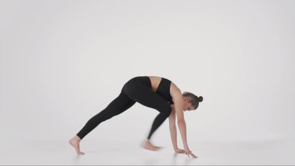 Joven flexible practicando poses Trikonasana y Downward Dog, estirando su espalda sobre fondo blanco del estudio - Metraje, vídeo