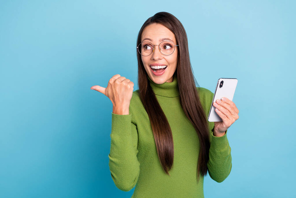 Photo of clever excited young woman wear green turtleneck glasses communicating modern device smiling isolated blue color background - Fotó, kép
