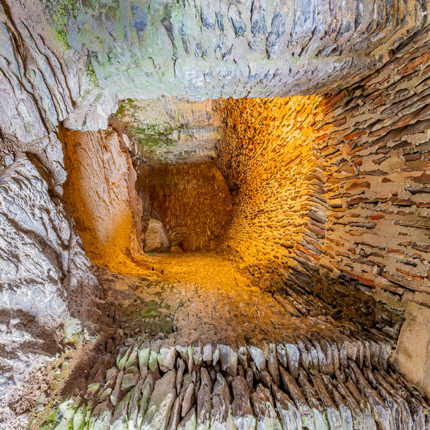 Mały korytarz lub tunel między ścianami, podłoga i sufit zniszczonych kamieni, mech i oświetlone żółtym światłem, ściana w tle, zamek Bourscheid, Luksemburg. Perspektywa głębokości - Zdjęcie, obraz