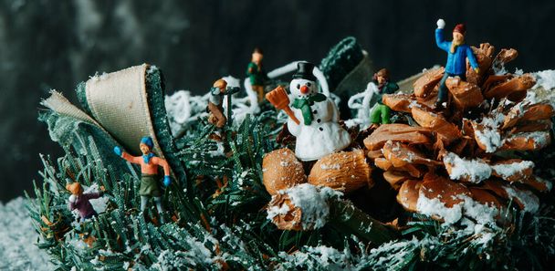 zbliżenie niektórych miniaturowych ludzi bawiących się na sztucznym śniegu w świątecznym wieńcu, w panoramicznym formacie używanym jako baner internetowy lub nagłówek - Zdjęcie, obraz