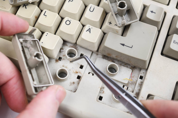 Computer keyboard with keys removed for cleaning.Men's hands clean the dust between the keys with tweezers. - Foto, afbeelding