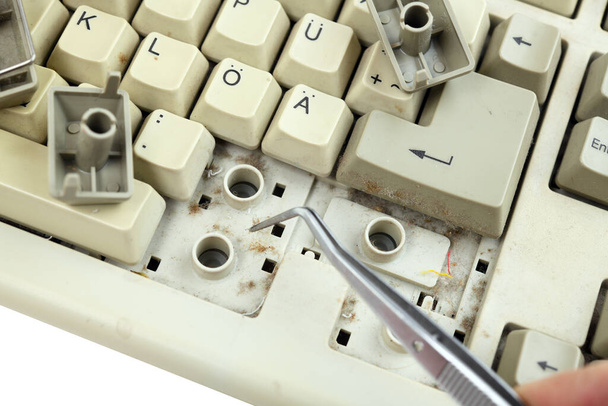 Computer keyboard with keys removed for cleaning.Men's hands clean the dust between the keys with tweezers. - Foto, afbeelding