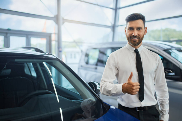 Knappe man die duim omhoog terwijl het kopen van auto bij salon - Foto, afbeelding