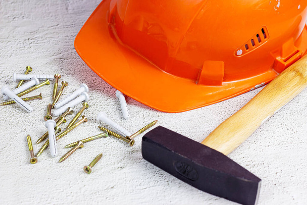 Oranje beschermende harde hoed met klauwhamer op lichtgrijs cement. Reparatie en verbetering van woningen, woningbouwconcept. - Foto, afbeelding