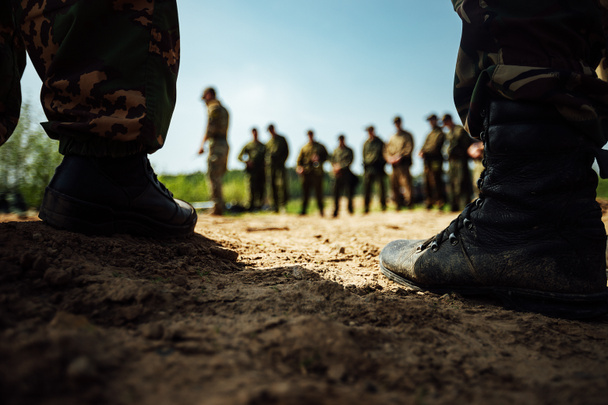 los pies de los soldados en botas del ejército están de pie sobre la arena. campo de entrenamiento antes de una larga marcha - Foto, Imagen