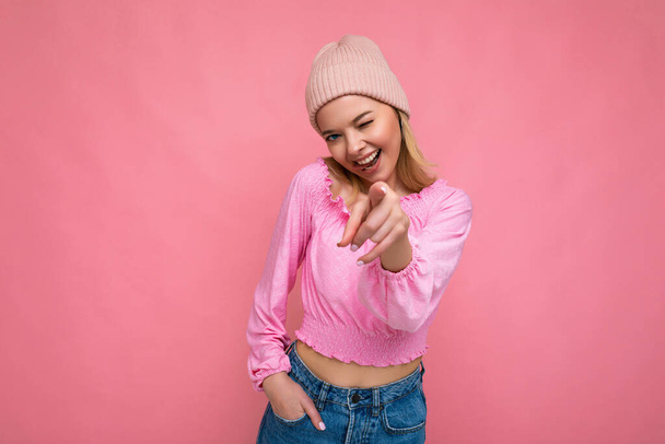 Photo of young positive happy smiling beautiful woman with sincere emotions wearing stylish clothes isolated over background with copy space and pointing at camera - Фото, зображення