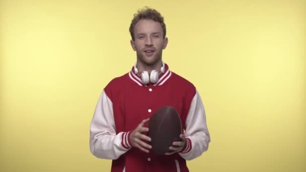 giovane in giacca bomber in possesso di palla da rugby su giallo  - Filmati, video