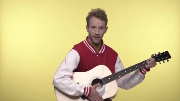young man in bomber jacket playing acoustic guitar and singing on yellow - Footage, Video